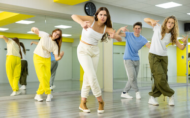 Emotional teenage girls and boys having group dance training in studio, performing dynamic elements