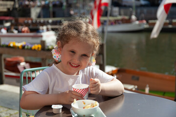 happy little girl sitting in an outdoor cafe. Embankment  along the Leie river with medieval houses...