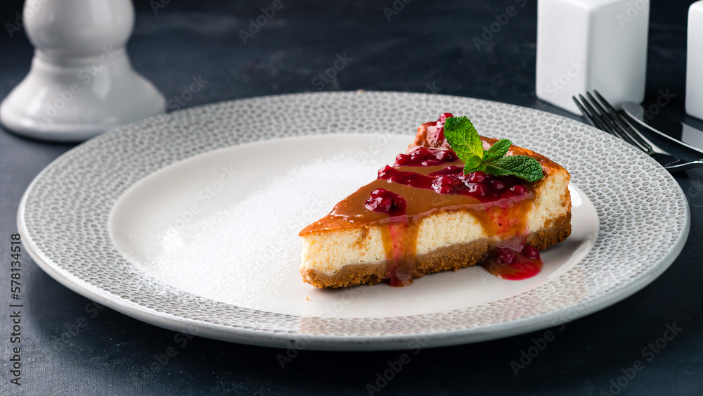 Sticker piece of caramel cheesecake with berry jam and mint in a plate.