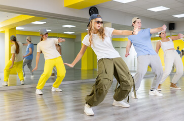 Cool active teenage girls and boy learning dance movements during group training in dance studio