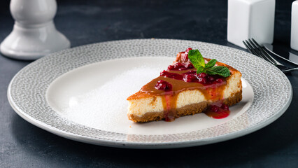 Piece of caramel cheesecake with berry jam and mint in a plate.