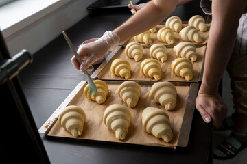 The baker brushes raw formed croissants with egg yolk before baking. Croissant production in the bakery