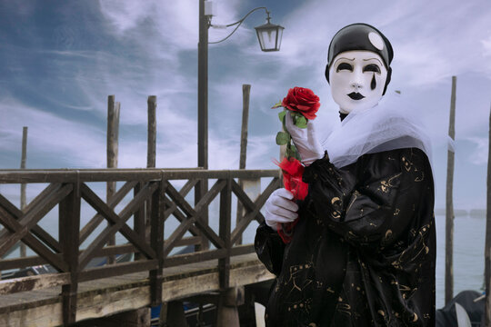 VENICE, Italy - February 17th 2023: Pierrot pierrot with rose in hand in the background Venice lagoon, Carnival mask.