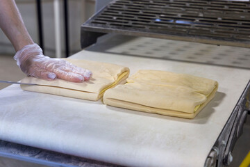 Baker in gloves prepares pastry dough in the press machine. Automation of dough production in the...