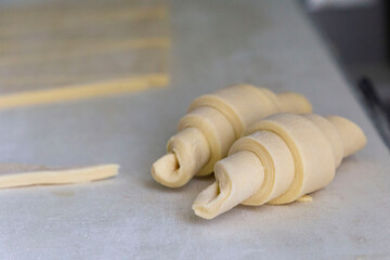Closeup of half-done uncooked croissant with sliced dough nearby