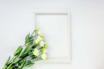 Blank picture frame and white eustoma flowers on white background. Valentines day, Mothers day, Womens day concept. Top view, flat lay, mock up