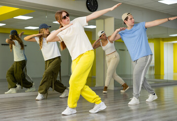 Group of teenagers in casual clothes training hip-hop in class, posing and having fun
