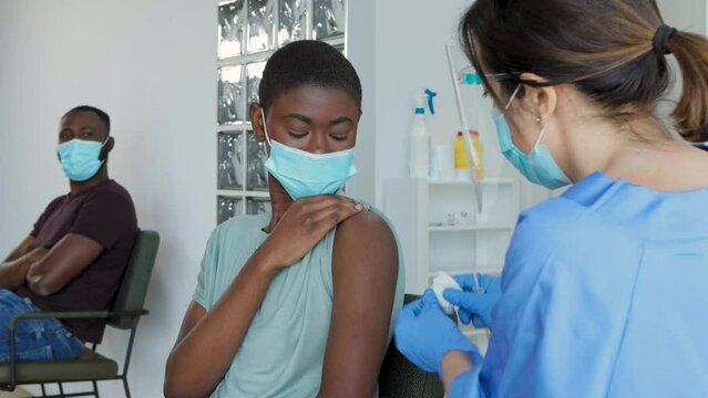 Medical specialist in protective uniform vaccinates an African female patient