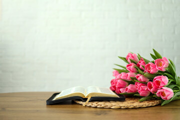 Open bible with tulip flowers on light wood