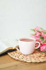 Open bible with tulip flowers and a cup of tea on light wood