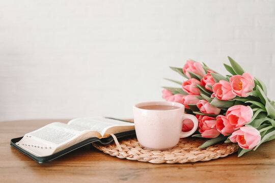 Open bible with tulip flowers and a cup of tea on light wood