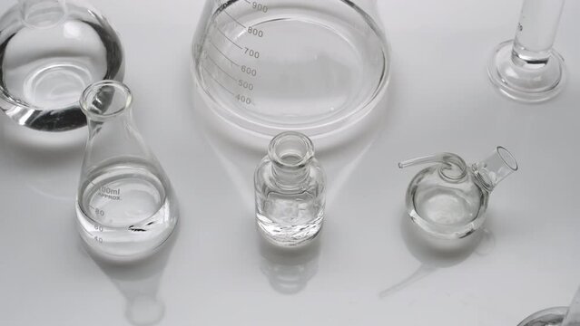 Close-up crane shot of lab glassware with water on grey background | Background shot for skincare products commercial