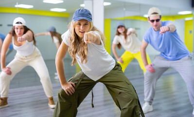 Active teenage girl with cap practicing breakdance Toprock moves in training hall. Teenagers engaged in breakdance