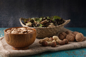 Rustic still life of dried fruits, roasted almonds in wooden bowl, peanuts, walnuts, hazelnuts and green dried flowers