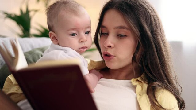 Portrait of cute young family spend leisure time together when mother reading book literature to her little baby soothes the child with his pleasant voice laying on sofa at light room