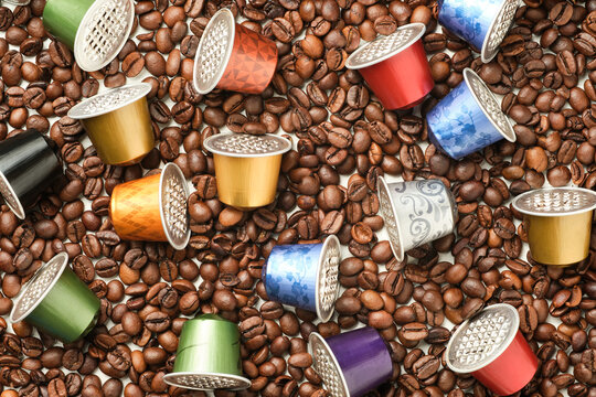 image from above of colored coffee capsules on surface full of coffee beans