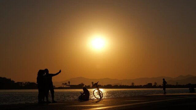 Silhouettes of people at sunset near the water. Silhouettes of a cyclist, a fisherman and a girl taking pictures at sunset.
