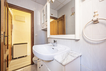 Fototapeta na wymiar Small bathroom with white porcelain sink with veined marble base, framed mirror, light tile and sapele wood doors