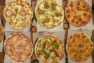 Thin crust Italian family pizzas with mushrooms, prosciutto, tomatoes, cheeses, sauces, vegetables, pepperoni and lots of basil on a wooden table