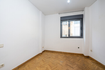 Empty room with herringbone-laid oak parquet flooring, gray aluminum window and white walls