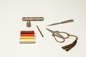 A set of old style copper scissors, thimbles and sewing accessories along with spools of multi colored thread on a plain white background