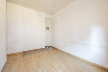 Empty room with poorly installed oak floor, white aluminum window and dirty white walls and marks of old furniture