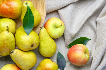 Overturned bowl of fresh pears and apples on fabric background, closeup
