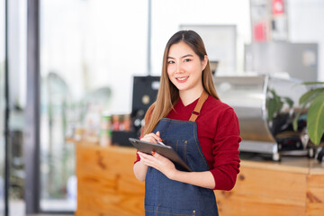 Opening a small business, AHappy Asian woman in an apron standing near a bar counter coffee shop, Small business owner, restaurant, barista, cafe, Online, SME, entrepreneur, and seller concept
