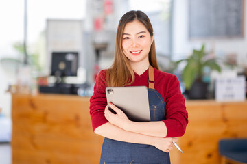 Opening a small business, AHappy Asian woman in an apron standing near a bar counter coffee shop, Small business owner, restaurant, barista, cafe, Online, SME, entrepreneur, and seller concept
