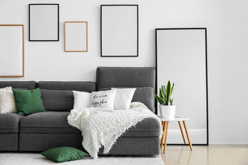 Interior of living room with black sofa, houseplant and blank frames