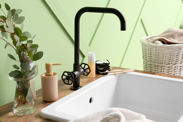 Fototapeta na wymiar Table with ceramic sink, bath accessories and eucalyptus in vase near green wall