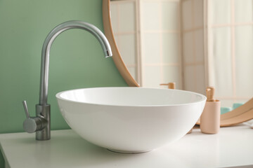 Ceramic sink and bath accessories on table near mirror