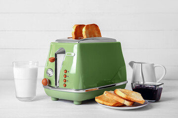 Modern toaster with crispy bread slices, glass of milk and jam on white table