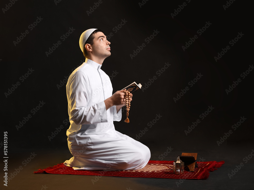 Wall mural Praying Muslim man with Koran on dark background