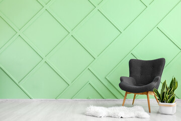 Stylish grey armchair, houseplant and white fur rug near green wall