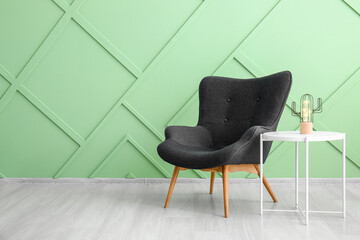 Stylish grey armchair and table with glowing lamp near green wall