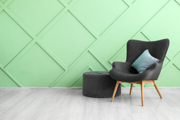 Stylish grey armchair, cushion and pouf near green wall