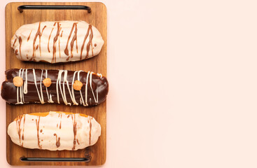 Board with delicious eclairs on pink background