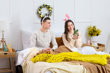 Happy young couple with bunny ears and Easter rabbit in bedroom