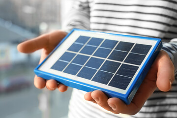 Young man with portable solar panel at home, closeup