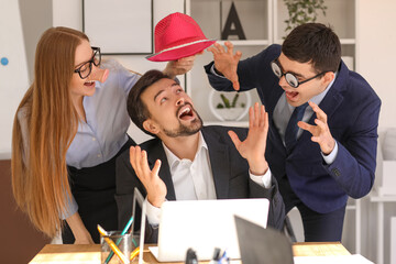 Colleagues with funny disguise putting hat on their boss in office. April Fools' Day celebration