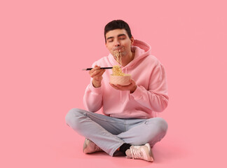 Young man eating Chinese noodles on pink background