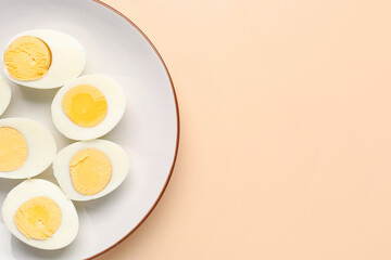 Plate with halves of delicious boiled eggs on beige background
