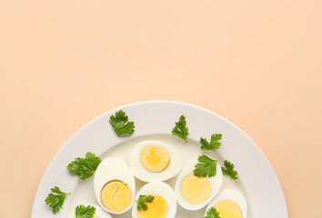Plate with halves of delicious boiled eggs and parsley on beige background
