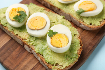 Board with delicious avocado toasts, boiled eggs, parsley and tomatoes on blue background