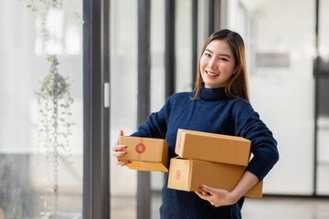 Startup small business entrepreneur of freelance Asian woman using a phone with box Cheerful success Asian woman her hand lifts up online marketing packaging box and delivery SME idea concept