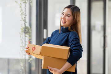 Startup small business entrepreneur of freelance Asian woman using a phone with box Cheerful success Asian woman her hand lifts up online marketing packaging box and delivery SME idea concept