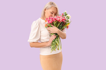 Beautiful mature woman with bouquet of flowers on lilac background