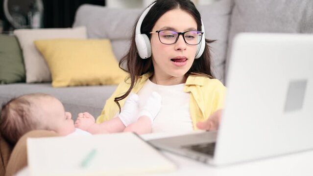 Portrait of busy young business mother holding her baby while working or studying on laptop computer and make notes at light home office Successful woman balancing work or education and motherhood