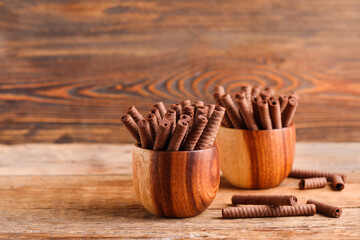 Bowls with delicious chocolate wafer rolls on brown wooden table